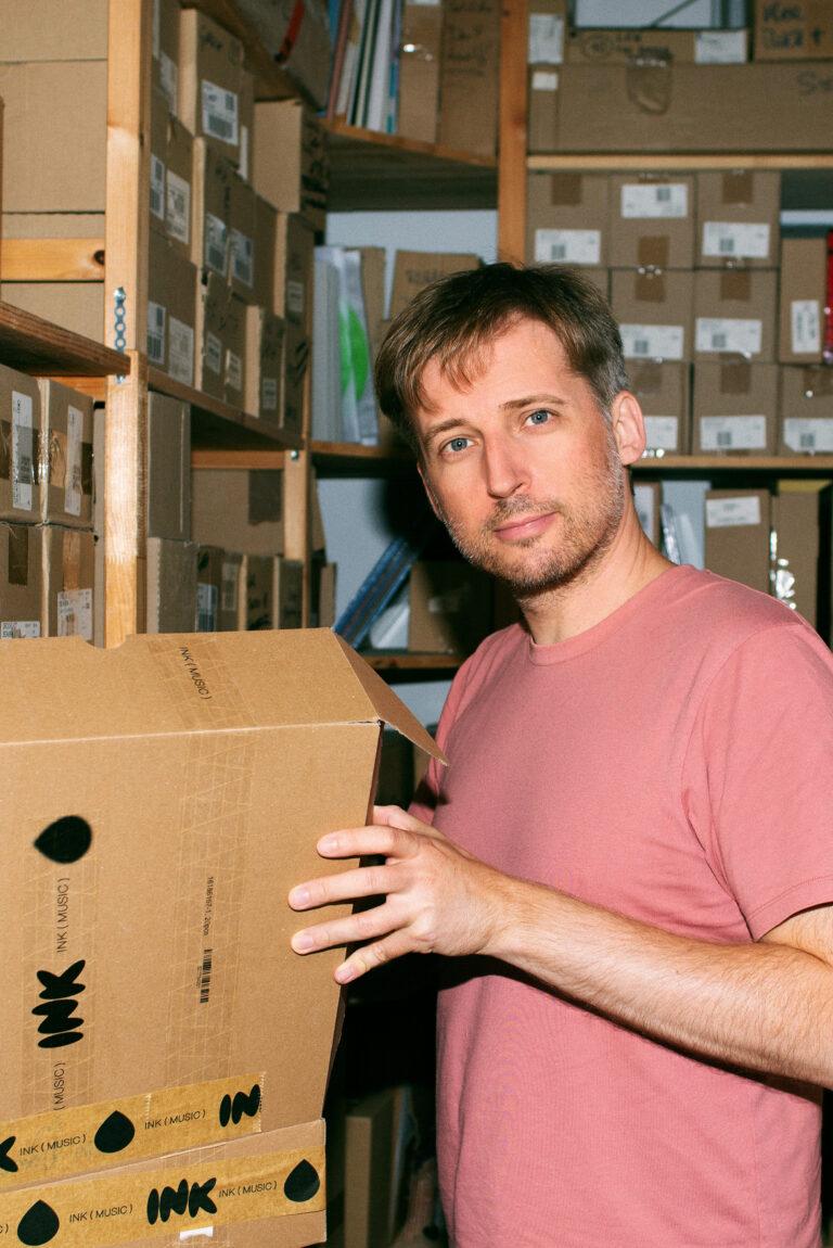 Ink Music - Teamfoto - Hannes Tschürtz - Mann steht vor einem Karton und blickt direkt in die Kamera